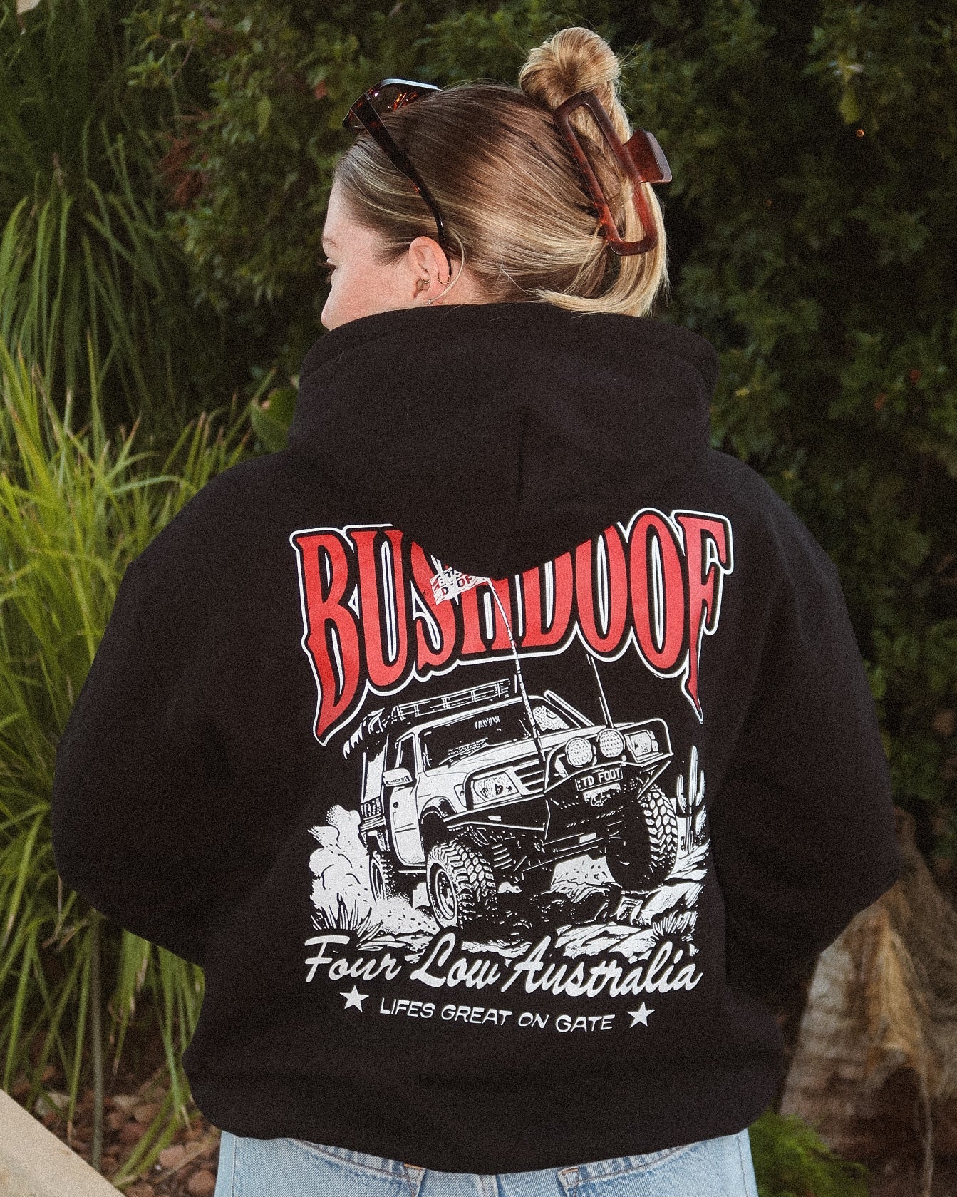 Person wearing a black hoodie with 'Bushdoof' and off-road vehicle design, standing outdoors.